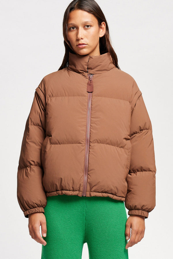 Model wearing the Transform Puffa Jacket on toffee side with sleeves attached, zipped up, showcasing cropped length and high collar