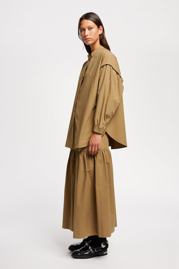 Side view of the Model wearing the Transit Gathered Blouse in Dusty Olive a relaxed band collar shirt with dropped shoulders, pleated sleeves, and a curved hemline.