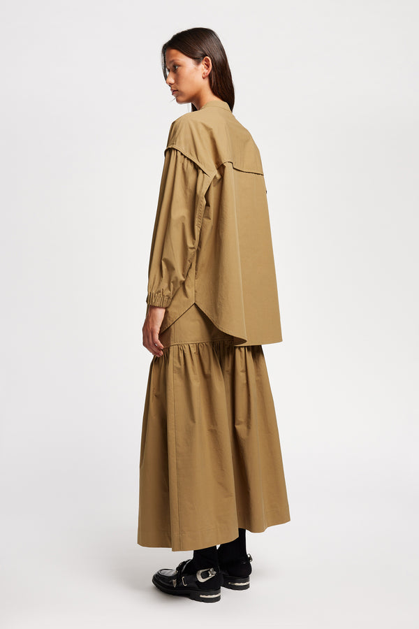 Back Angle view of the Model wearing the Transit Gathered Blouse in Dusty Olive a relaxed band collar shirt with dropped shoulders, pleated sleeves, and a curved hemline.