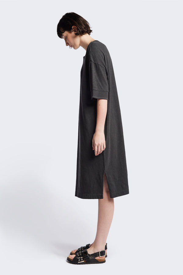 Side of The Treatise Henley Dress in Black soft jersey, featuring a relaxed boxy fit, crew neckline, henley button detail, and falling just below the knee. Available in 5 sizes.