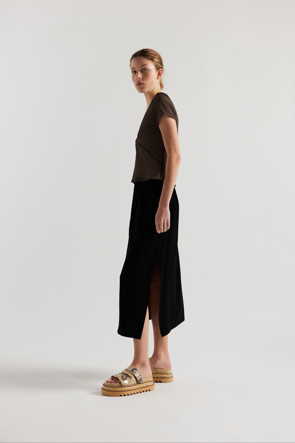 Side view on model of Mid-length slip skirt in black soft viscose-rayon. Ft. elasticated gathered waist with self-tie pull and side split visible.