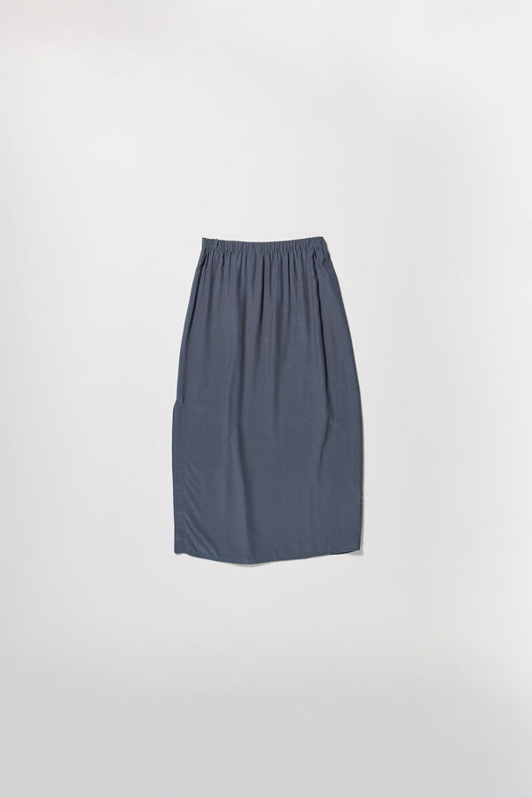 Flat front of Mid-length slip skirt in indigo soft viscose-rayon. Ft. elasticated gathered waist with self-tie pull and side split visible.