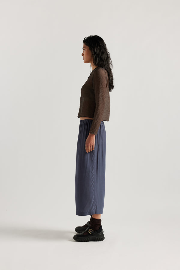 Side view on model of Mid-length slip skirt in Indigo soft viscose-rayon. Ft. elasticated gathered waist with self-tie pull and side split visible.