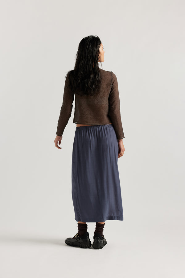 Back view on model of Mid-length slip skirt in Indigo soft viscose-rayon. Ft. elasticated gathered waist with self-tie pull and side split visible.
