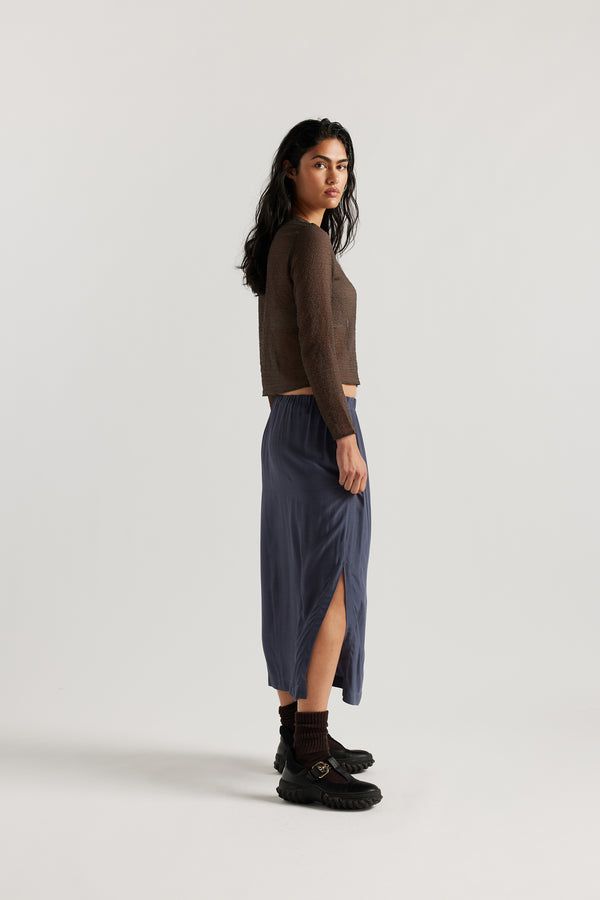 Side view on model of Mid-length slip skirt in Indigo soft viscose-rayon. Ft. elasticated gathered waist with self-tie pull and side split visible.