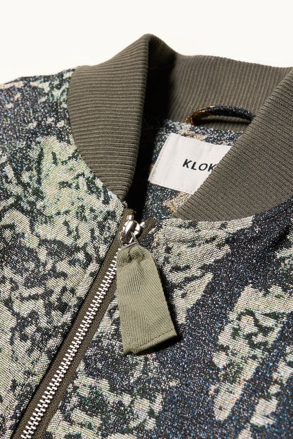 Close up fabric and collar detail shot of Unisex bomber jacket in Green Print woven jacquard with real tree camouflage, featuring dropped shoulders, ribbed trims, and full-length front zip.