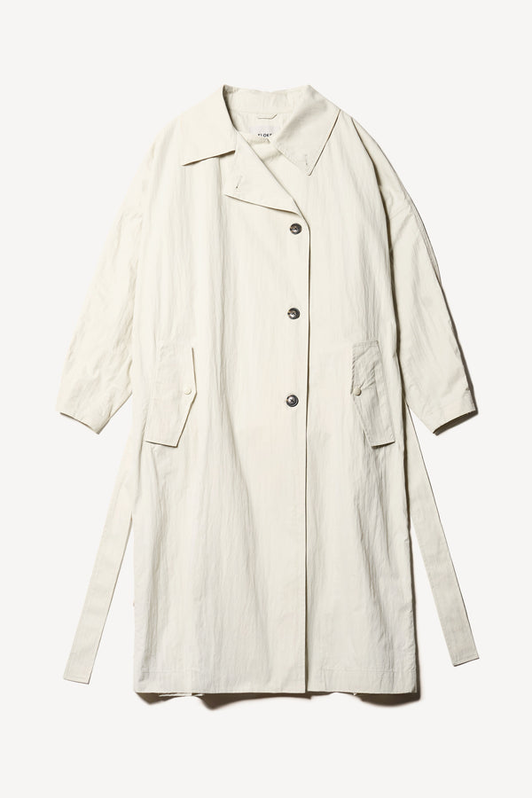 Flat Front of the Volt Trench in Bone, collar up. A lightweight double-breasted trench coat with flap pockets