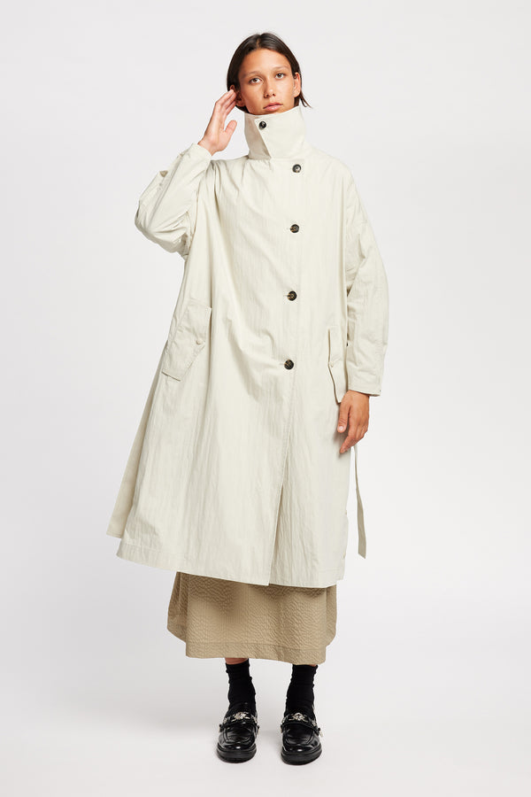 Front view of model wearing the Volt Trench in Bone collar up. A lightweight double-breasted trench coat with flap pockets