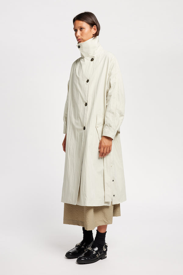 Side angle view of model wearing the Volt Trench in Bone collar up. A lightweight double-breasted trench coat with flap pockets