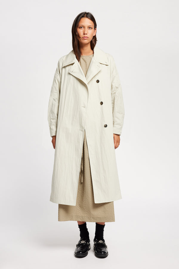 Front view of model wearing the Volt Trench in Bone collar down. A lightweight double-breasted trench coat with flap pockets