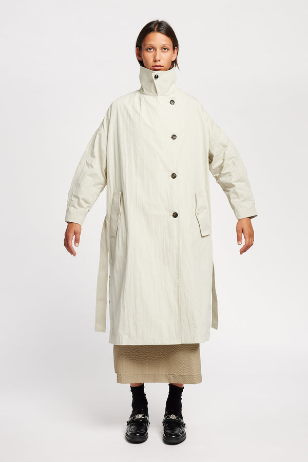 Front view of model wearing the Volt Trench in Bone collar up. A lightweight double-breasted trench coat with flap pockets