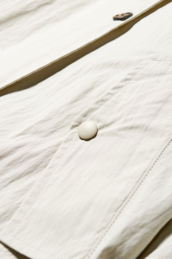 Close up detail button and pocket shot of the Volt Trench in Bone. A lightweight double-breasted trench coat with flap pockets