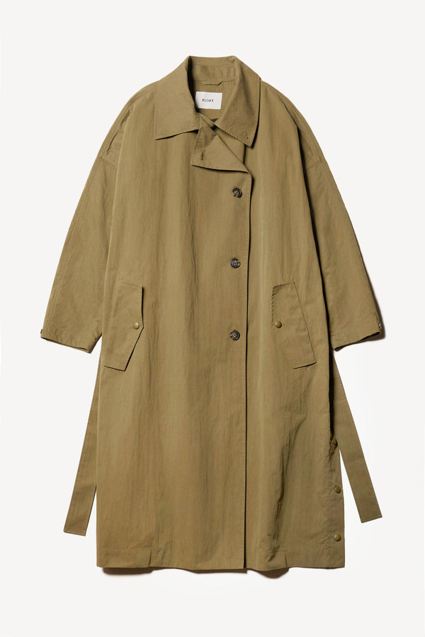 Flat Front of the Volt Trench in Kelp Green, collar up. A lightweight double-breasted trench coat with flap pockets