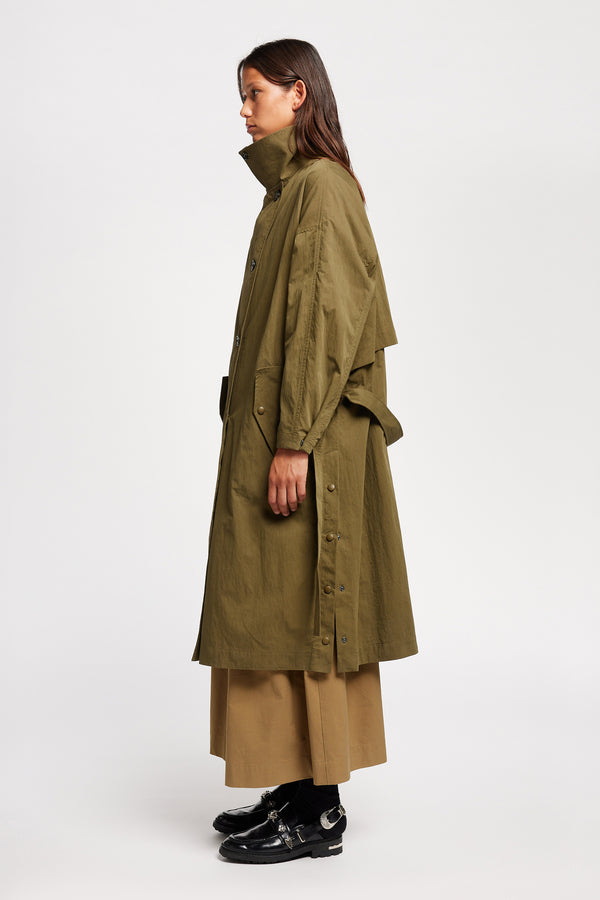 Side view of model wearing the Volt Trench in Kelp Green, collar up. A lightweight double-breasted trench coat with flap pockets