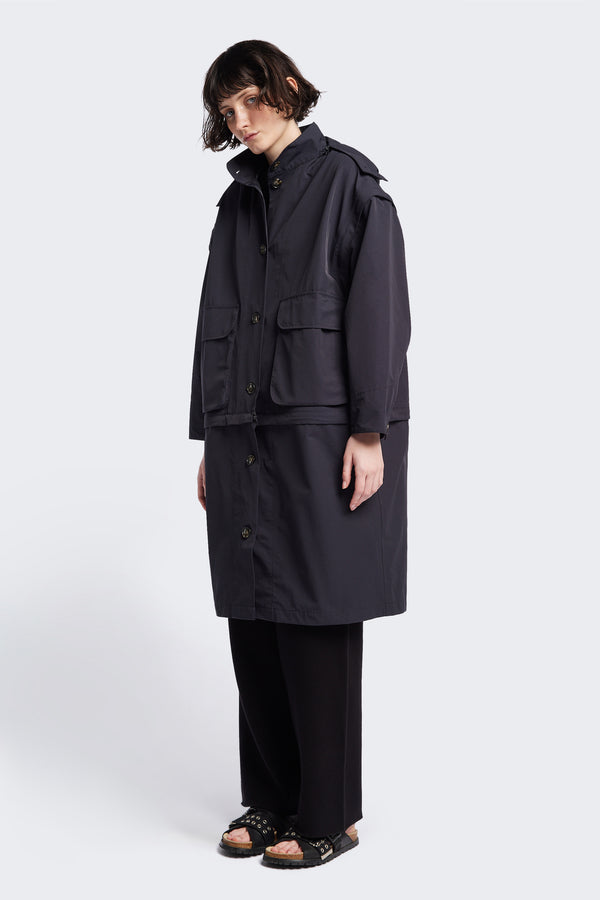 Front of the Vulcan Zip Coat in black, an oversized, six-in-one waterproof design with zip-off sleeves and bottom, featuring 3D front pockets, a detachable hood, and a stand collar.