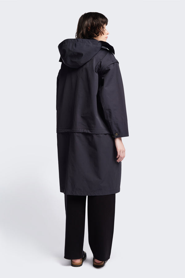 Back of the Vulcan Zip Coat in black, an oversized, six-in-one waterproof design with zip-off sleeves and bottom, featuring 3D front pockets, a detachable hood, and a stand collar.