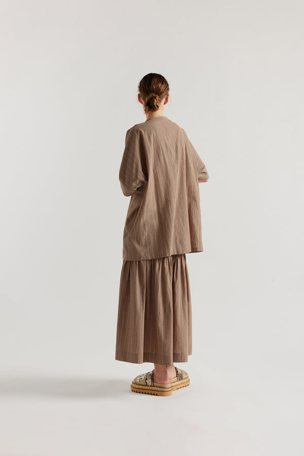 Back view of model in the oversized boxy yarn-dyed cotton top with round crew neck and concealed placket in burnt orange, ecru and black stripe. 