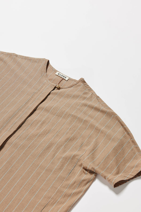 Close up detail shot of the oversized boxy yarn-dyed cotton top with round crew neck and concealed placket in burnt orange, ecru and black stripe. 