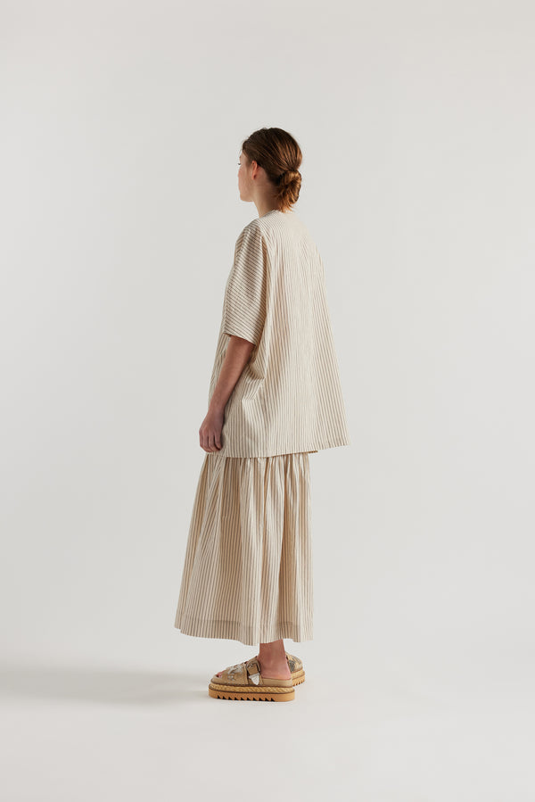 Back view of model in the oversized boxy yarn-dyed cotton top with round crew neck and concealed placket in Ecru with black pin stripe. 