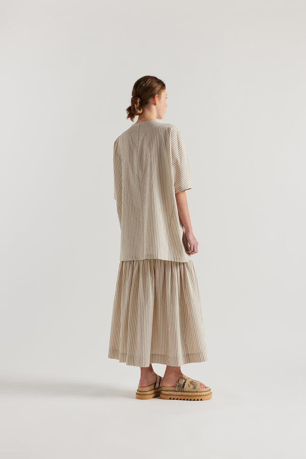 Back view of model in the oversized boxy yarn-dyed cotton top with round crew neck and concealed placket in Ecru with black pin stripe. 