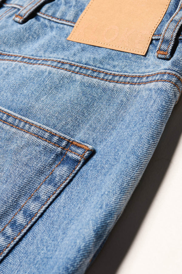 Close-up of Kloke straight-leg jeans in mid blue fade Japanese denim, showcasing five-pocket design and branded back patch.