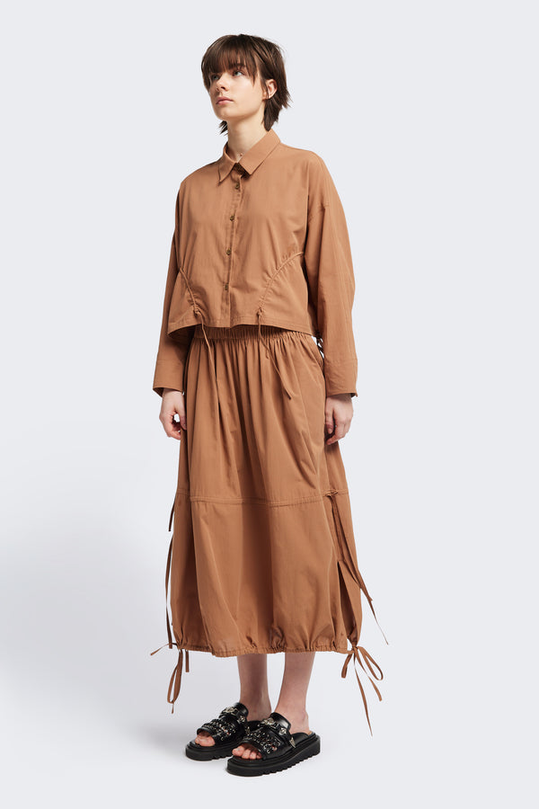 Front of The Repose Skirt in toffee brown with an elasticated waist, tuck and channel pull-through details, and an adjustable hem for a customisable silhouette.