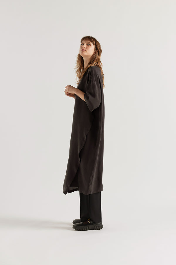 Side of Eon Dress in black layered over the Manta Pant showing daytime styling and fluid asymmetric midi silhouette.