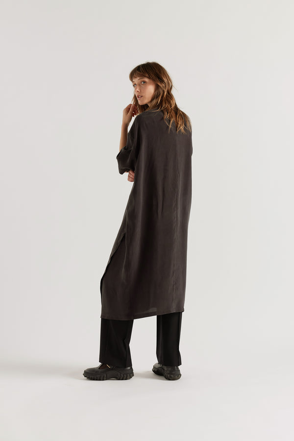 Back of Eon Dress in black layered over the Manta Pant showing daytime styling and fluid asymmetric midi silhouette.