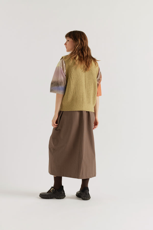 Back of model in Faint Knit Vest worn buttoned over a Top, showing sleeveless cut, 1x2 rib sleeve openings and reverse half-cardigan rib knit in RWS Merino