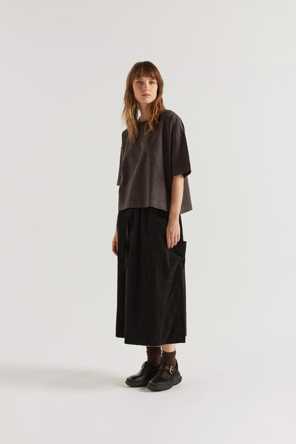 Black Fleeting Cord Skirt front view showing loose midi silhouette, panelled construction, scoop front pockets and double over-dyed corduroy