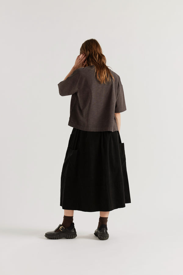 Back view of the Black Fleeting Cord Skirt showing loose midi silhouette, elasticated waistband with adjustable waist tie and double over-dyed corduroy