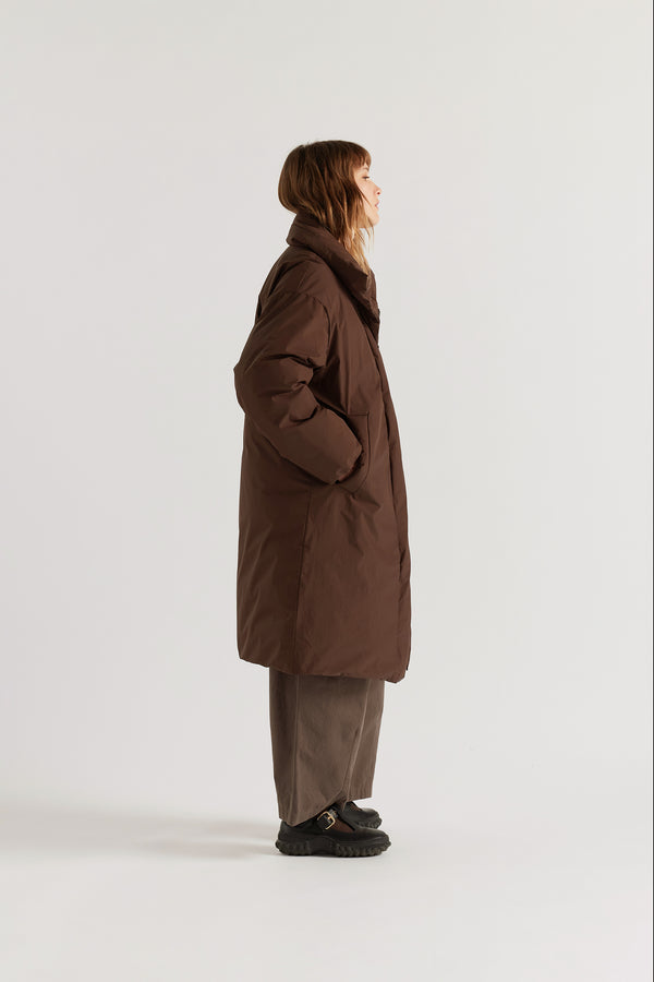 Side of model in Chocolate Brown Floating Puffa Coat worn closed, showing full-length silhouette, down-filled high collar and centre-front zip with magnetic fastenings