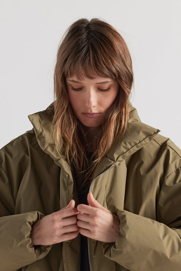 Front of  model in Olive Floating Puffa Coat worn, showing down-filled high collar and centre-front zip with magnetic fastenings