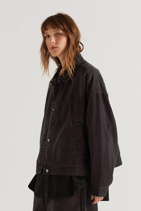 Front angle view of model in the black fade Oversized denim jacket with wide sleeves, deep welt pockets and a vintage-inspired over-dyed wash.