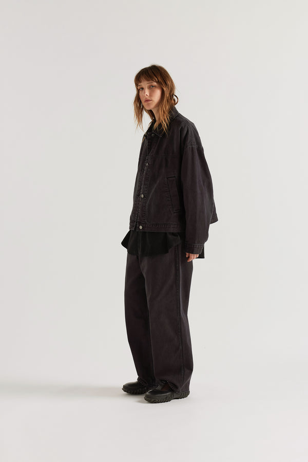 Front angle view of model in the black fade Oversized denim jacket with wide sleeves, deep welt pockets and a vintage-inspired over-dyed wash.