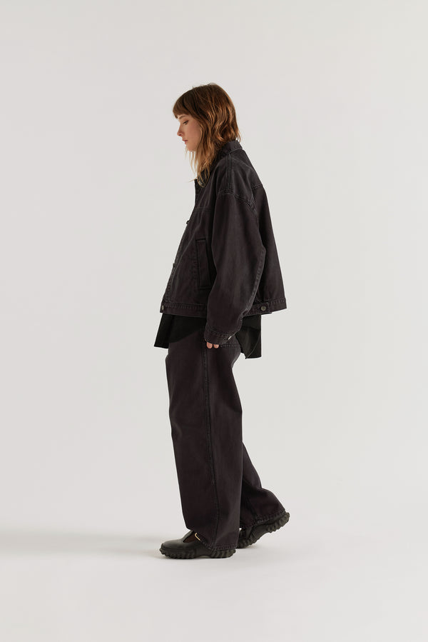 Side view of model in the black fade Oversized denim jacket with wide sleeves, deep welt pockets and a vintage-inspired over-dyed wash.