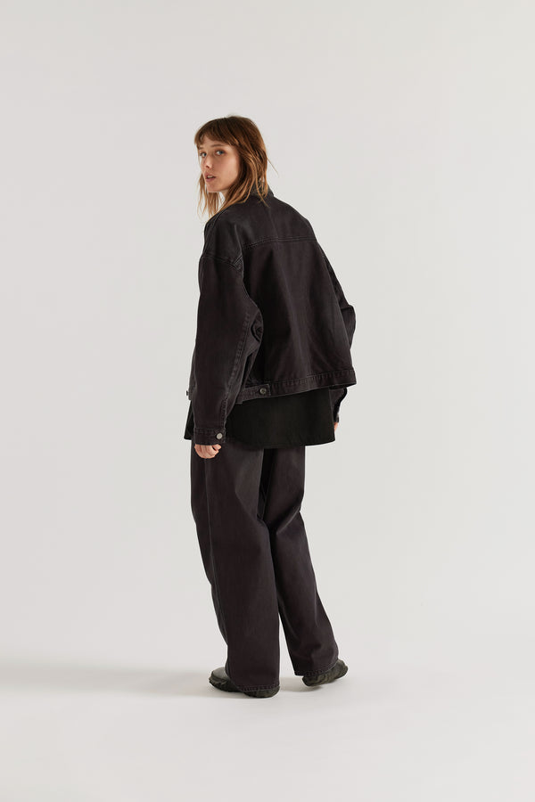 Back view of model in the black fade Oversized denim jacket with wide sleeves, deep welt pockets and a vintage-inspired over-dyed wash.