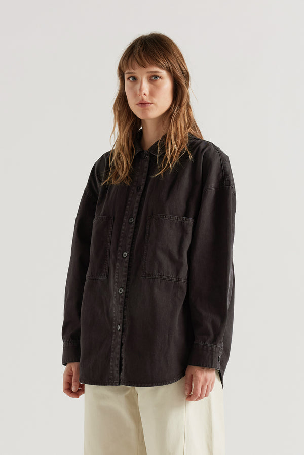 Front of model in the Black Fade Iris Denim Shirt with an oversized fit, dropped shoulders and utility-inspired chest pockets.
