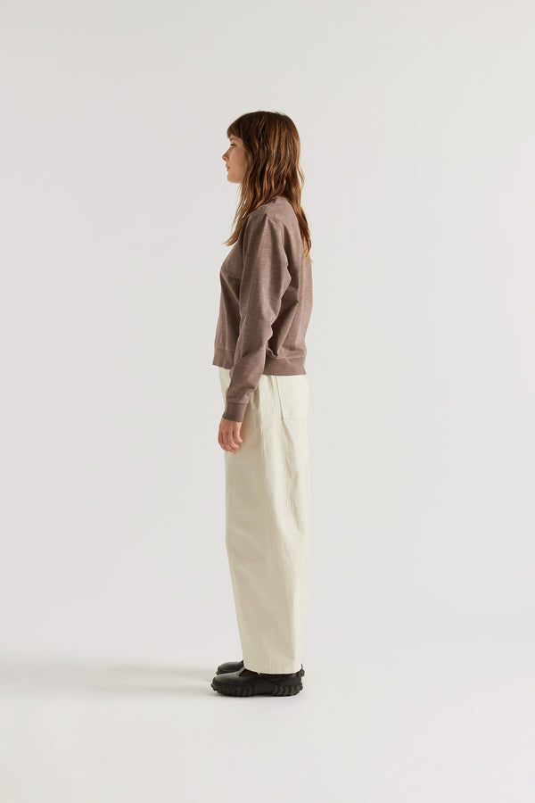 Side profile of female model in the brown Luster Long Sleeve Top featuring dropped sleeves and rib hem detailing.