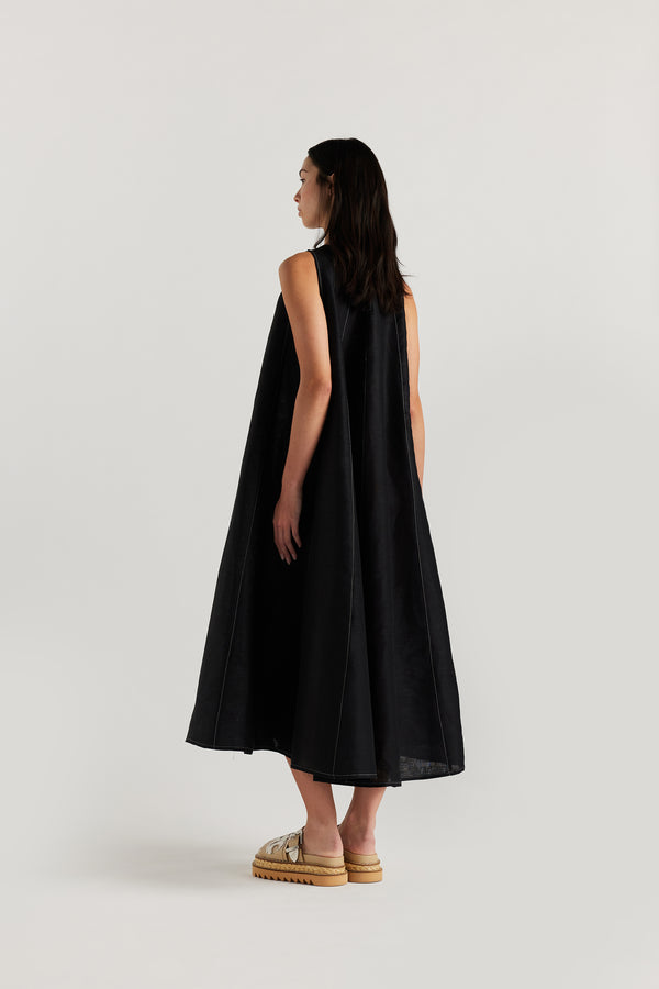 Back of the female model in the black linen dress featuring contrast stitching, vertical panel detailing and a subtle A-line silhouette.