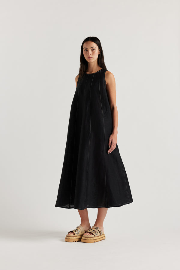 Front of the female model in the black linen dress featuring contrast stitching, vertical panel detailing and a subtle A-line silhouette.