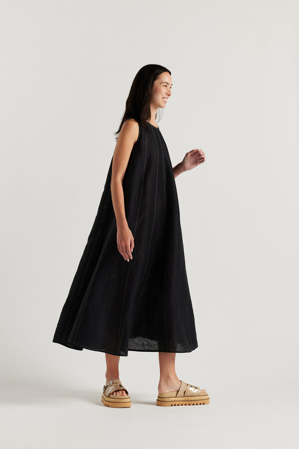 Front angle of female model in the black linen dress featuring contrast stitching, vertical panel detailing and a subtle A-line silhouette.