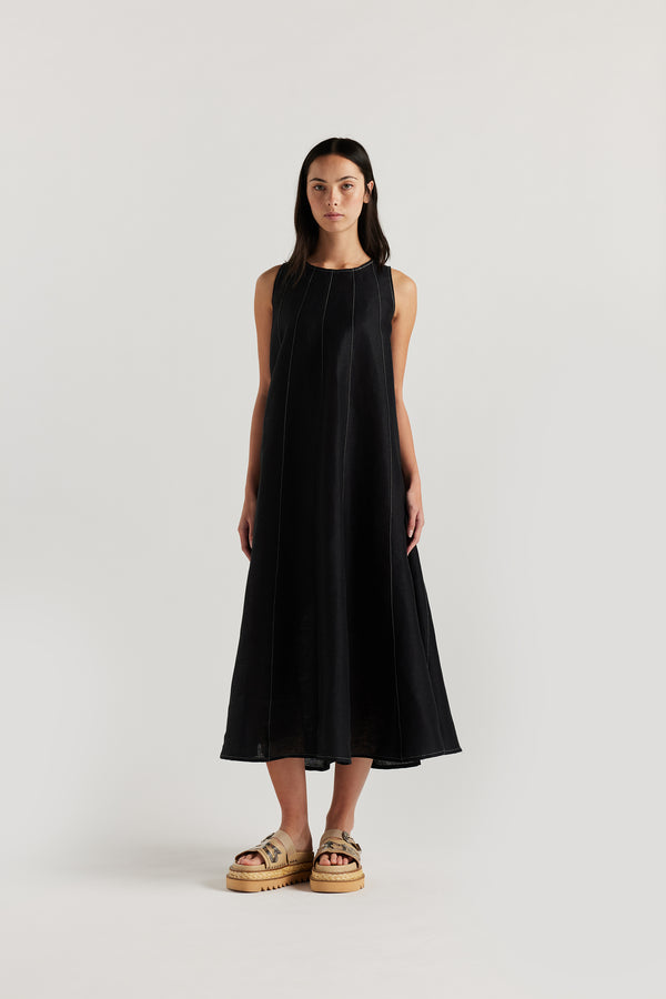 Front of the female model in the black linen dress featuring contrast stitching, vertical panel detailing and a subtle A-line silhouette.