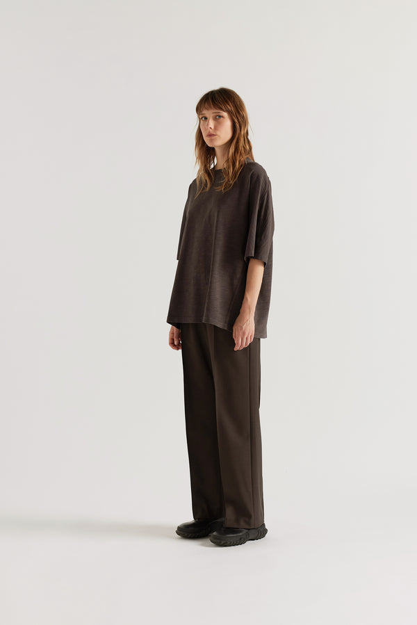 Front angle of female model in the black Overdyed Declare Tee in Nut Brown with a relaxed boxy fit and twisted sleeve detailing.