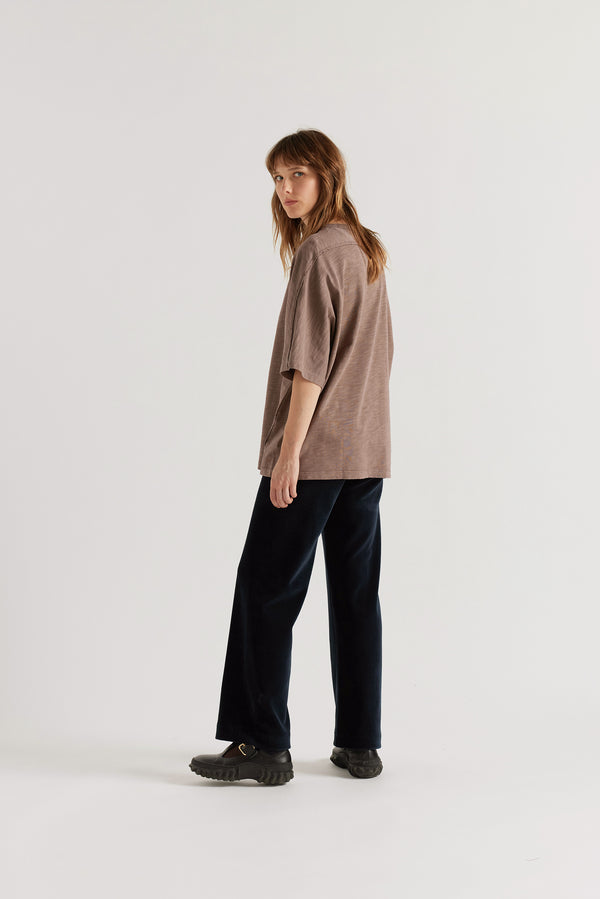 Back view of female model in the  brown Overdyed Declare Tee in Nut Brown showing the relaxed silhouette.