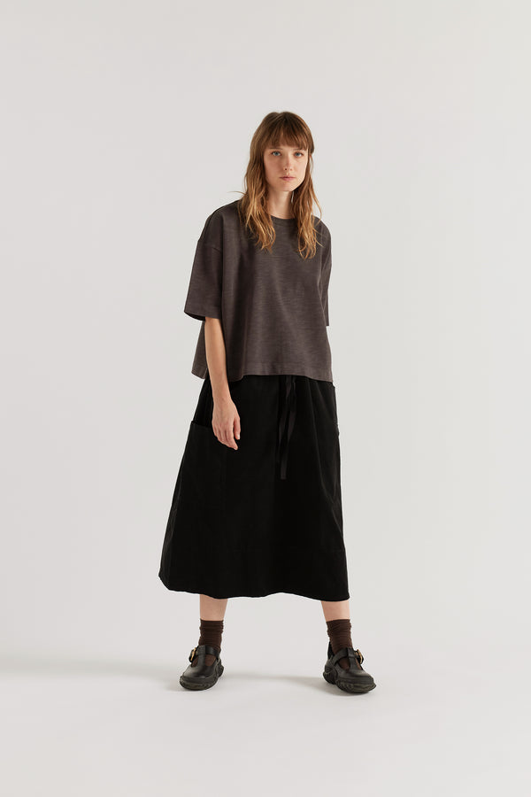 Front of the model in the licorice black Obelisk Tee in pigment-dyed cotton with a relaxed boxy fit and oversized elbow-grazing sleeves.