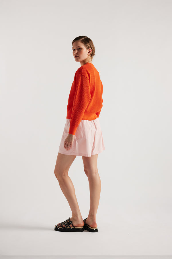 Model wearing KLOKE pointelle-knitted cotton sweater in dutch orange, back view