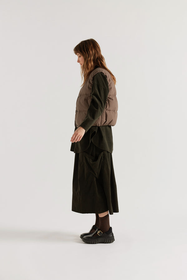 Side profile of female model in the brown quilted down vest showing the relaxed fit and elasticated armhole.
