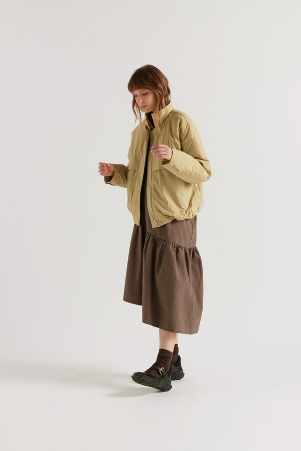 Front angle of female model in the Sand Beige Surge Quilted Jacket worn open, showing relaxed silhouette, military tab collar and storm flap pocket detailing