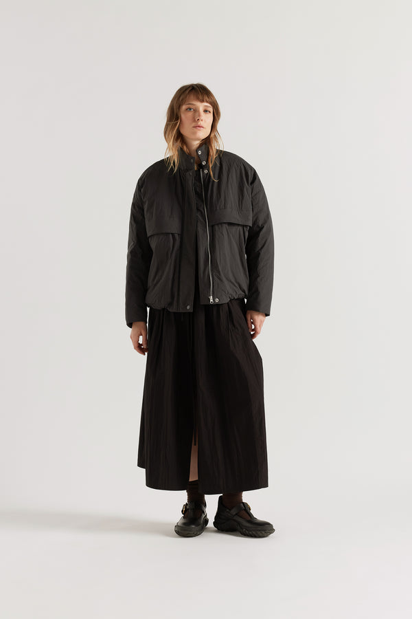 Front of female model in the black Surge Quilted Jacket worn open, showing relaxed silhouette, military tab collar and storm flap pocket detailing